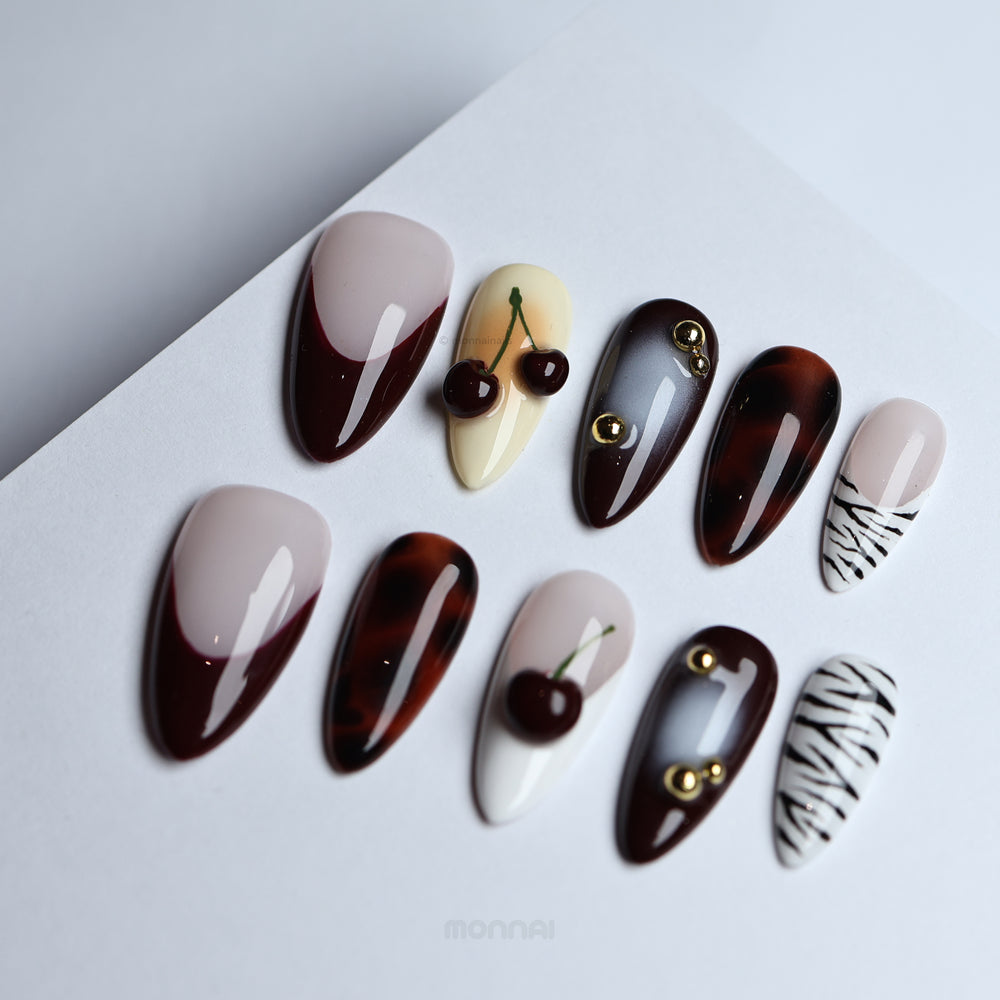 A Little Sweet press-on nails laid out with vintage tortoiseshell, cherry accents, deep brown French tips and zebra contrast.