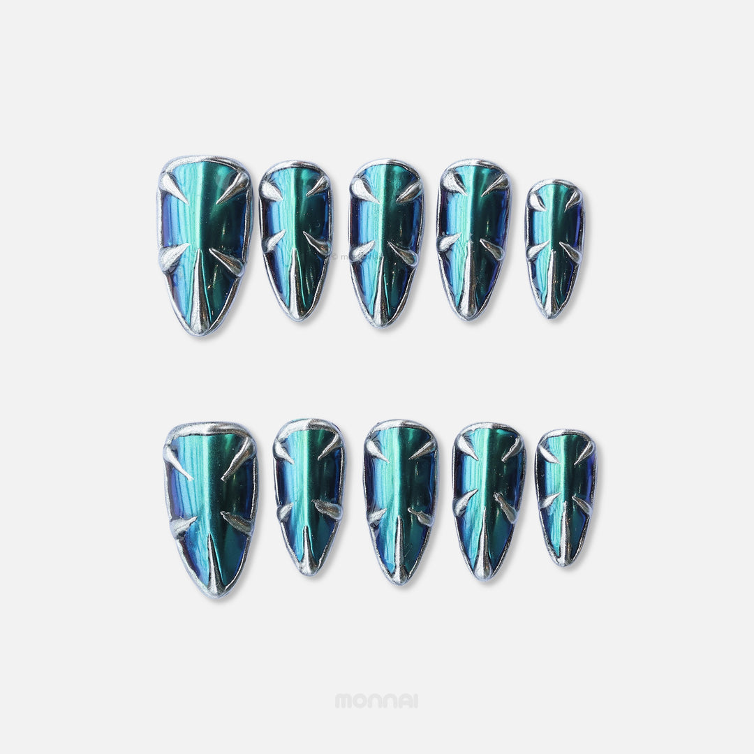 Alien press-on nails laid out in close-up, featuring teal and blue multichrome chrome with silver spiked metallic details.