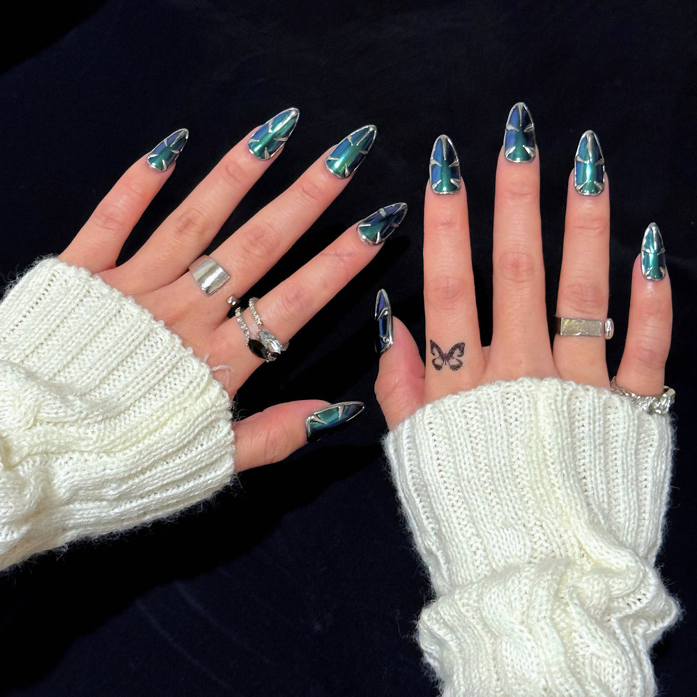 Alien press-on nails worn on hands, with teal and blue multichrome chrome and silver metallic edges in an edgy futuristic style.