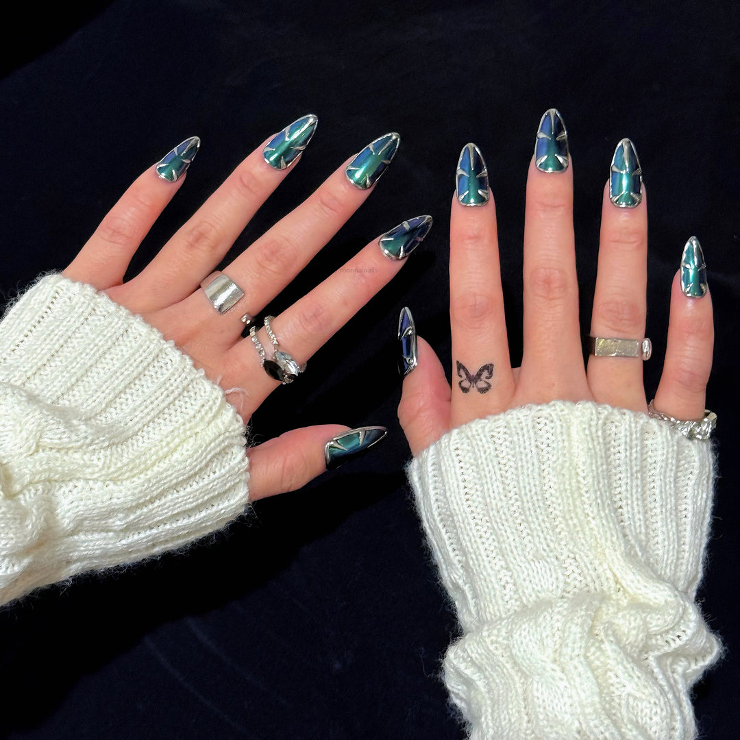 Alien press-on nails worn on hands, with teal and blue multichrome chrome and silver metallic edges in an edgy futuristic style.