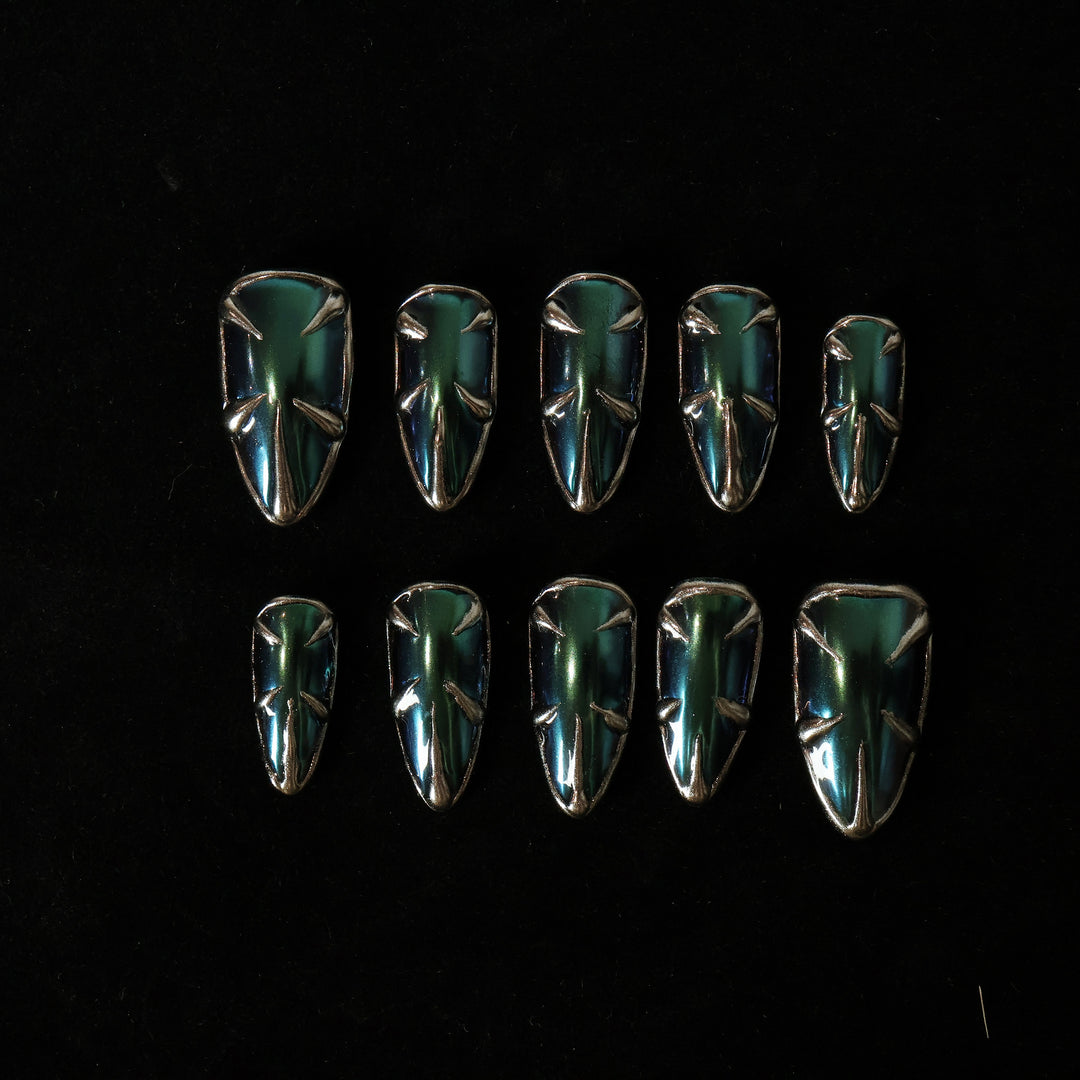 Alien press-on nails laid out, showing teal and blue multichrome metallic spikes and silver borders