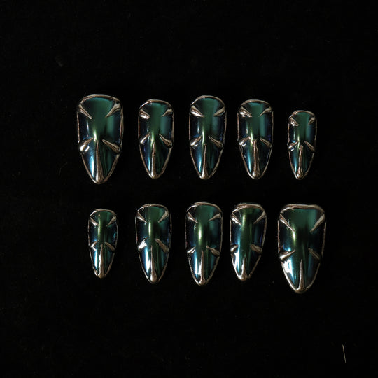 Alien press-on nails laid out, showing teal and blue multichrome metallic spikes and silver borders