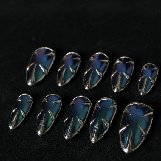 Alien press-on nails in blue-green multichrome with silver spikes, laid out in a sleek metallic futuristic style.