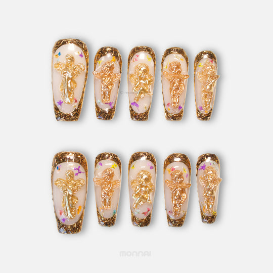 Angel Glow press-on nails shown in a set, with milky bases, gold cherub charms, and ornate metallic gold borders