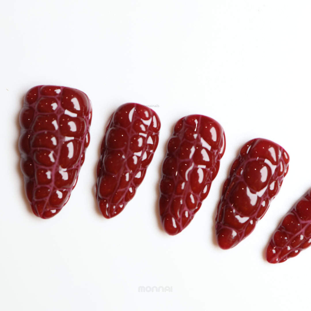 Antique Elegance press-on nails in rich dark red crocodile texture with a glossy finish, laid out in close-up.