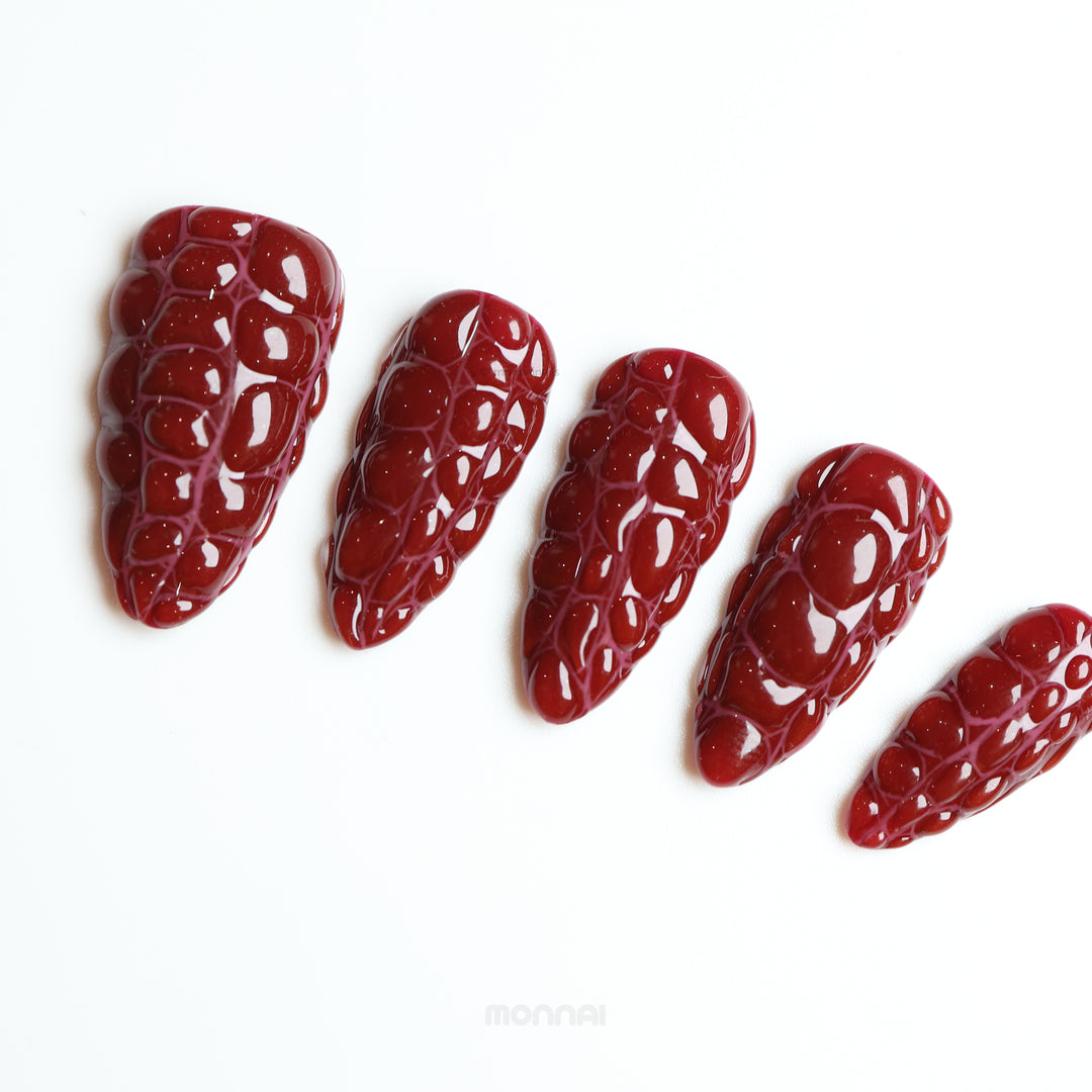 Antique Elegance press-on nails in dark red crocodile texture with glossy finish, shown laid out in close-up.