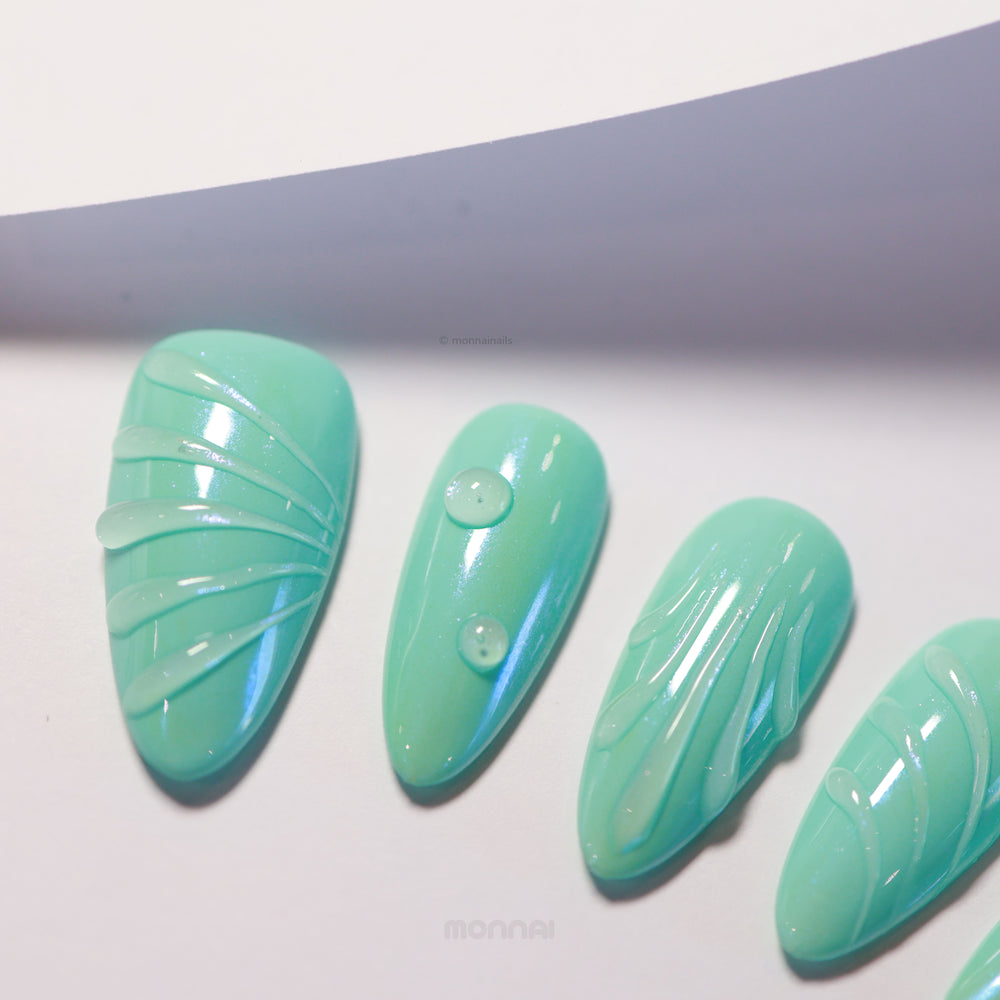 Aqua Glow press-on nails laid out with glossy teal bases, fine sculpted lines and droplet details