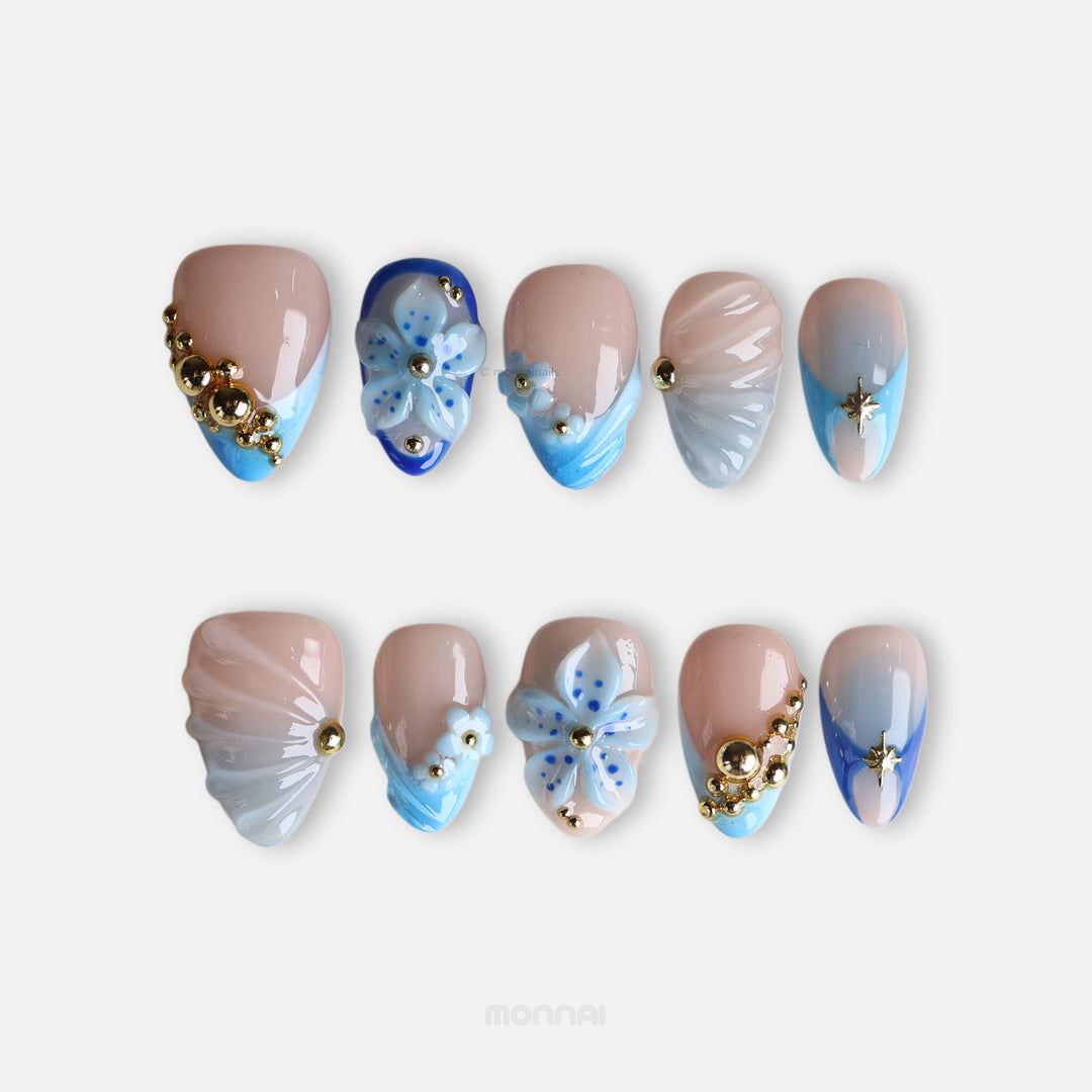 Aquamarine press-on nails laid out with nude bases, blue gradient tips, 3D flowers, gold beads, shells and star accents