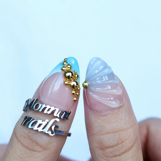 Aquamarine press-on nails on fingers with blue gradient tips, gold beads, and a sculpted shell design