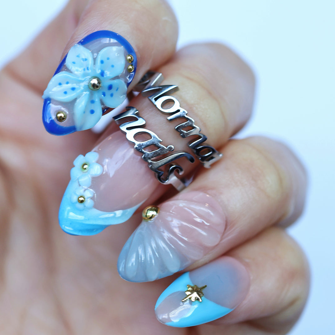 Aquamarine press-on nails on hand with blue gradient tips, 3D flower detail, gold beads, and seashell-like ridges