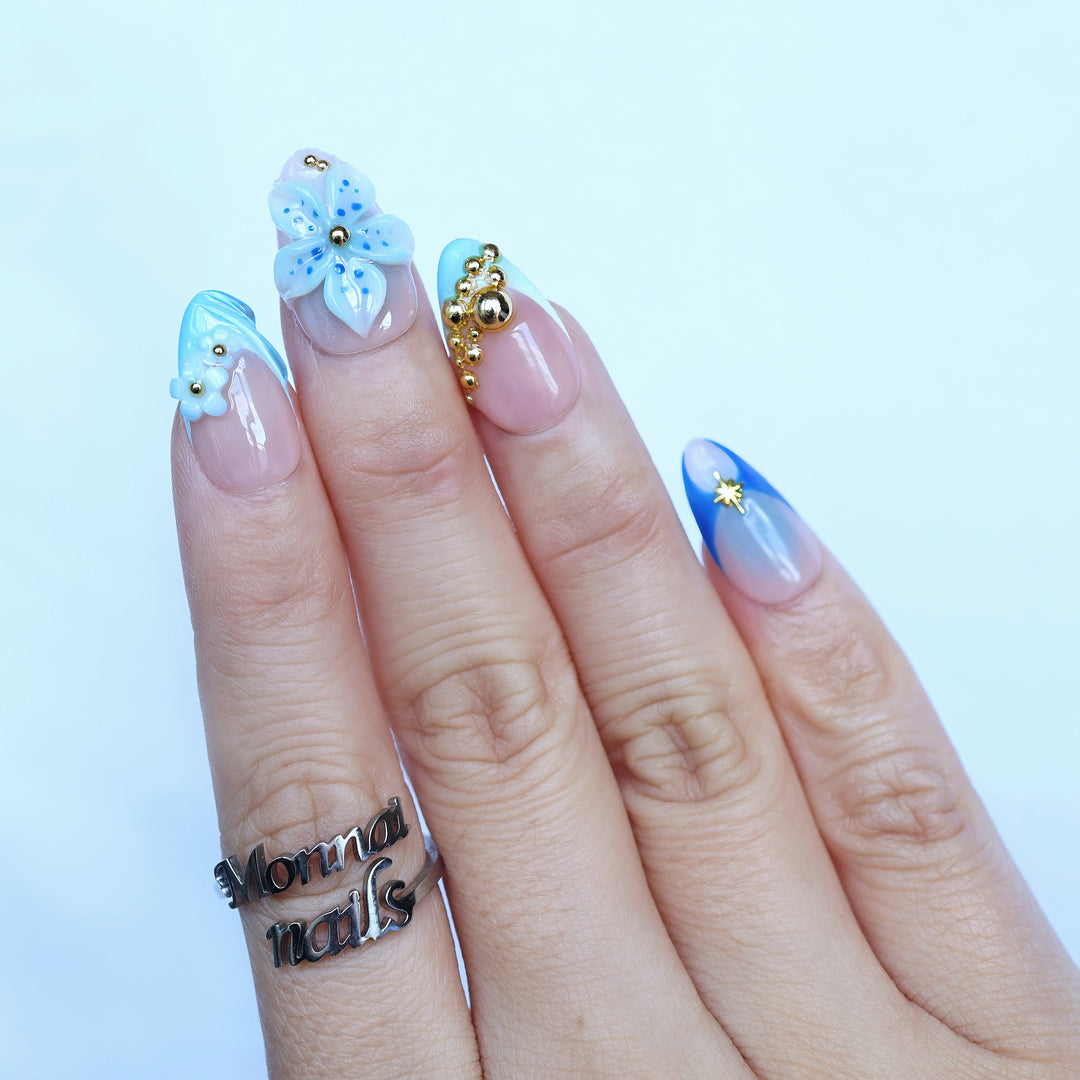 Aquamarine press-on nails on hand with blue gradient tips, 3D flowers, and gold bead accents