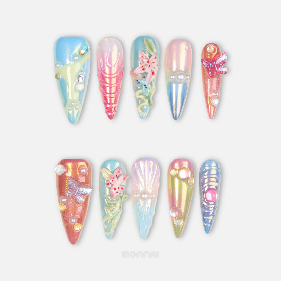 Aurora Cove press-on nails laid out, iridescent pastel shells with floral details, pearls, and butterfly accents