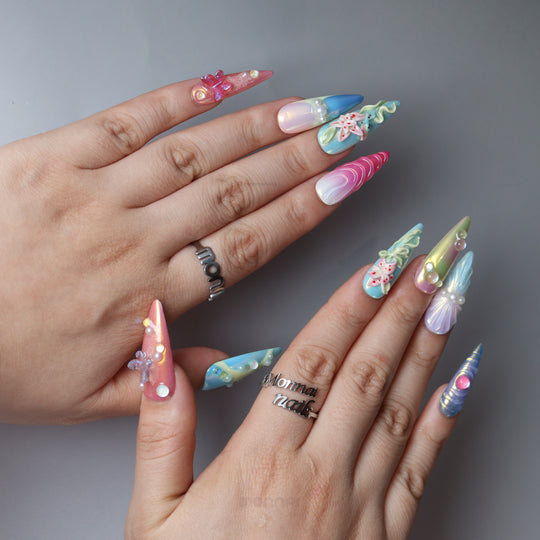 Aurora Cove press-on nails worn on hands, with iridescent pastel tones, floral details, pearls, and butterfly accents.