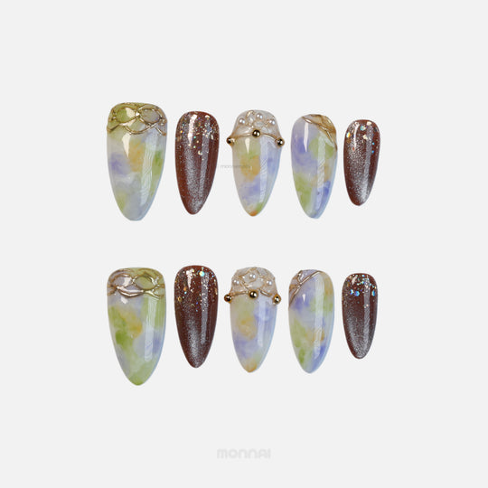 Aurora Veil press-on nails laid out in close-up, with green and lavender watercolor blending, brown shimmer, gold lines and pearl accents.