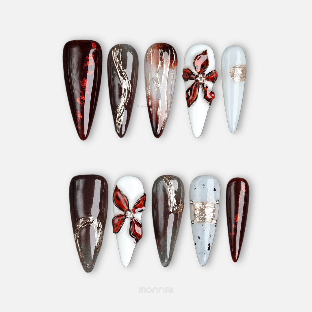 Autumn Elegance press-on nails shown in close-up, featuring deep brown, grey, and milky white designs with glossy floral and metallic accents.