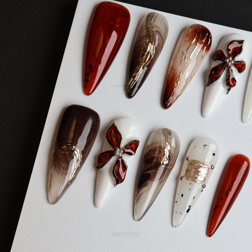 Autumn Elegance press-on nails in rich brown, grey, and white with glossy floral accents and metallic details, laid out on display.