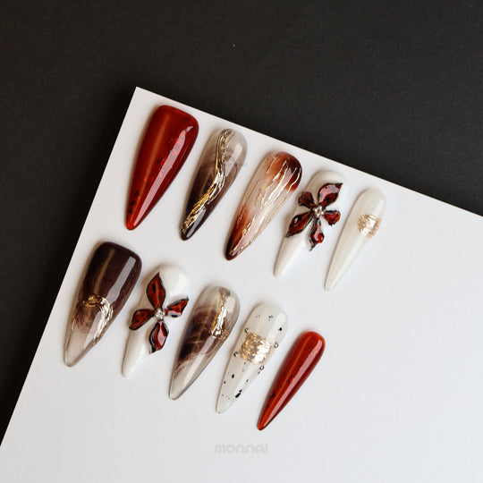 Autumn Elegance press-on nails laid out, with deep brown, milky white, and metallic floral accents.