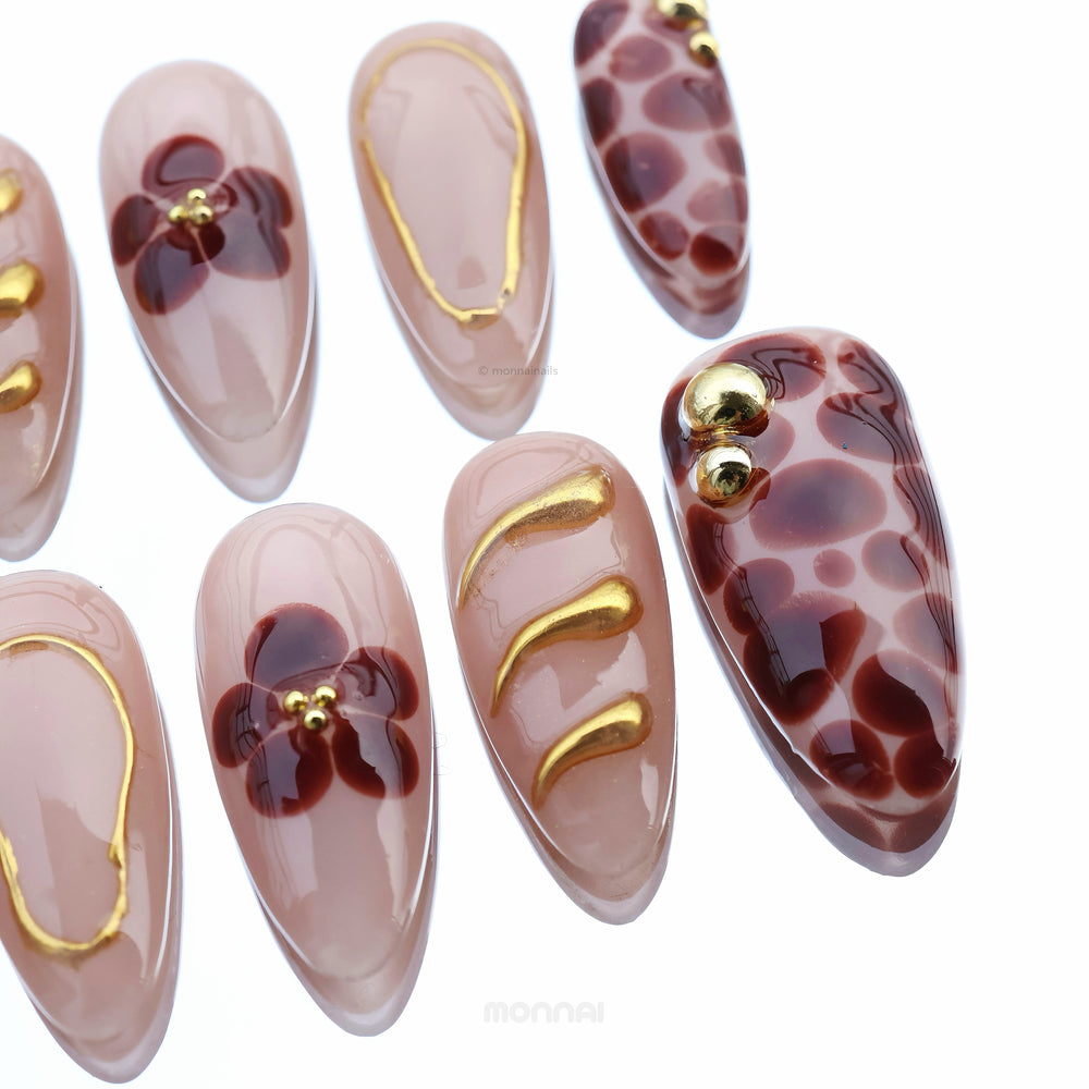 Autumn Touch press-on nails laid out in close-up, with sheer nude gloss, red florals, spotted accents and fine gold lines.