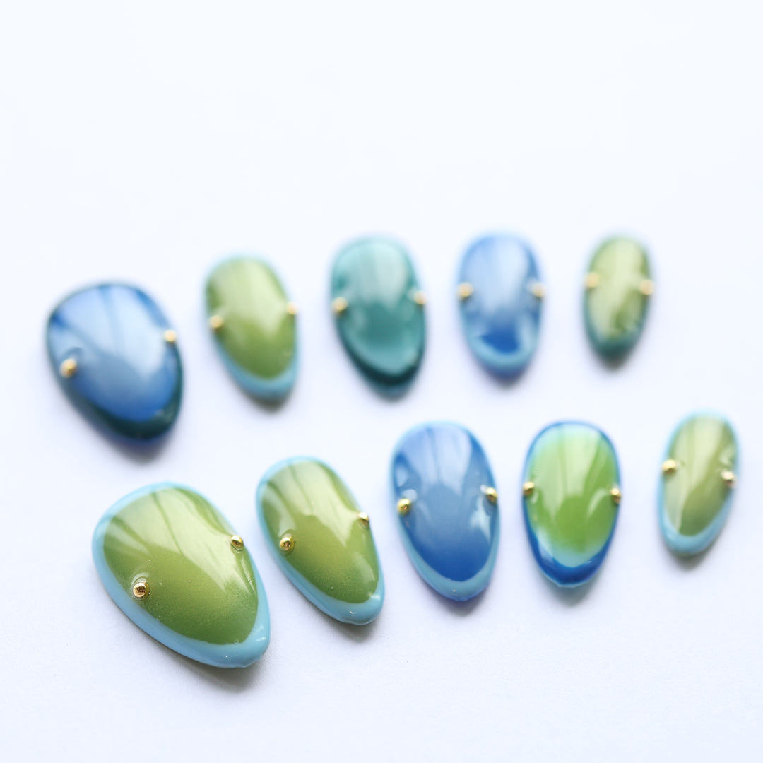 Azure Olive press-on nails laid out with blue-green gradient and gold studs on a white background