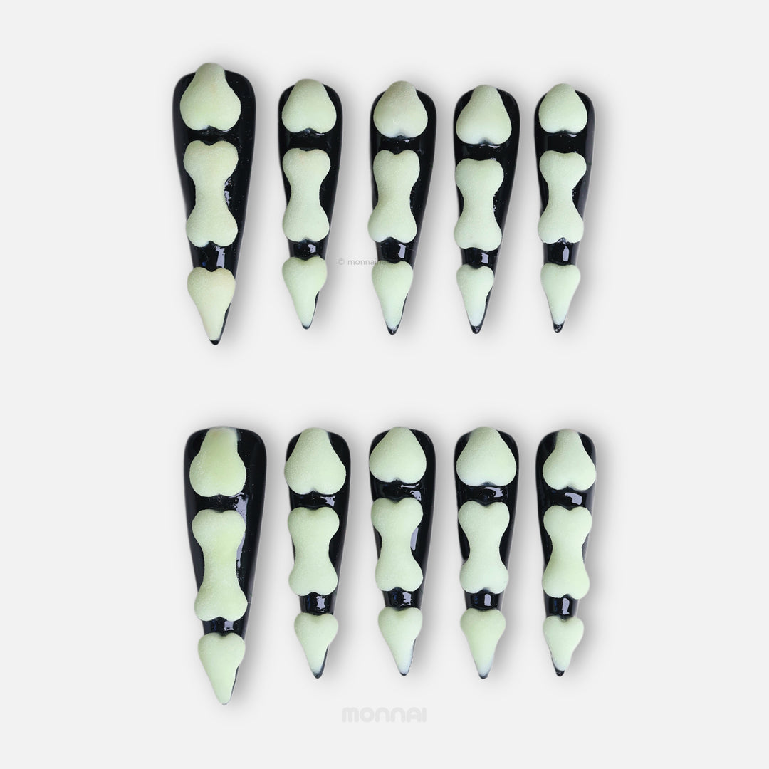 Bad to the Bone press-on nails laid out, black gothic nails with glow-in-the-dark bone segments and a matte finish.