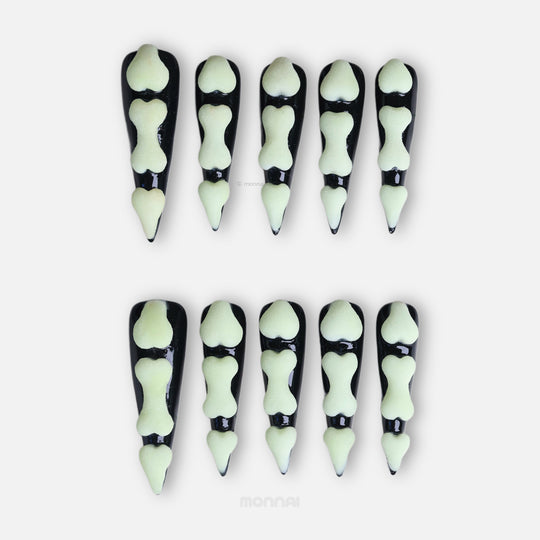 Bad to the Bone press-on nails laid out, black gothic nails with glow-in-the-dark bone segments and a matte finish.