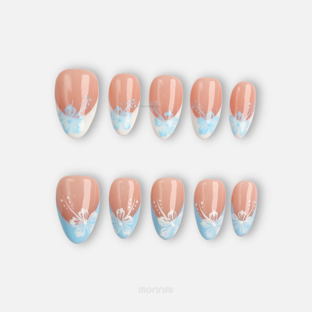 Barely Blue press-on nails laid out, nude French tips with powder blue floral details and white accents