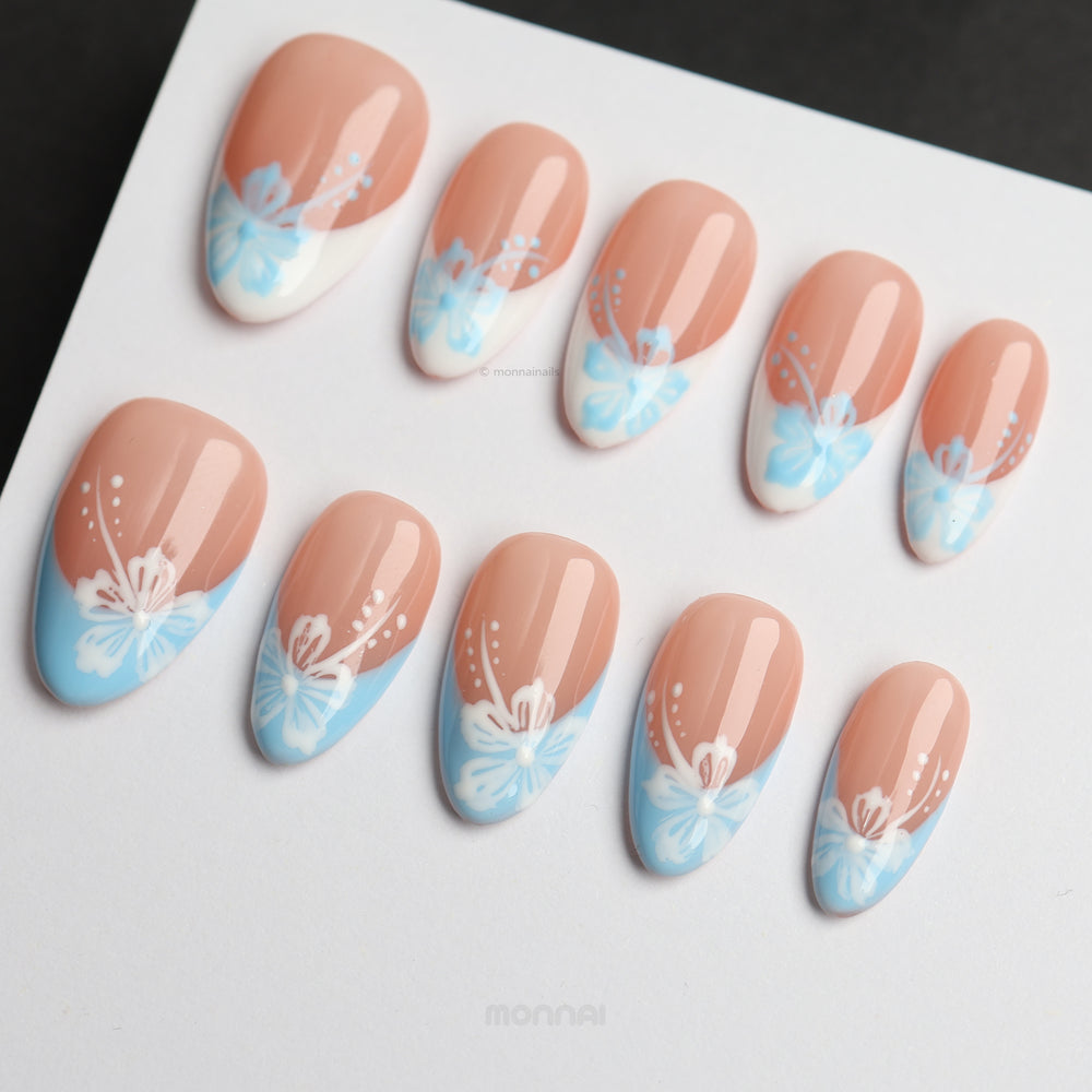 Barely Blue press-on nails laid out with soft nude French tips, powder blue florals, and white dotted accents