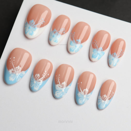 Barely Blue press-on nails laid out with soft nude French tips, powder blue florals, and white dotted accents