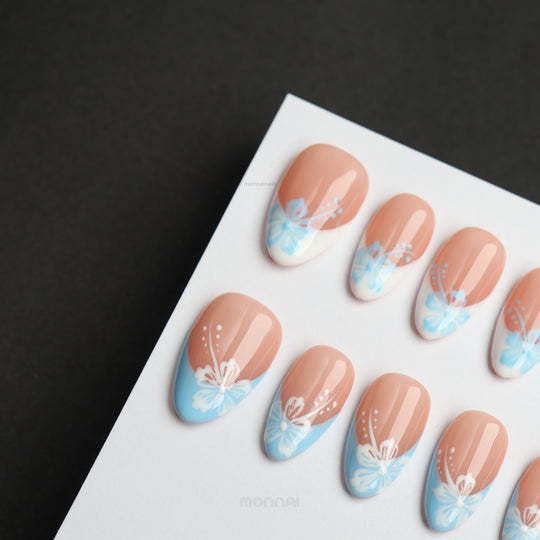 Barely Blue press-on nails laid out, with nude bases, powder blue tips, and white floral dotted accents