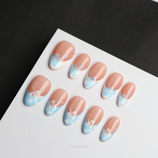 Barely Blue press-on nails laid out with soft nude, powder blue French tips, and white floral accents.