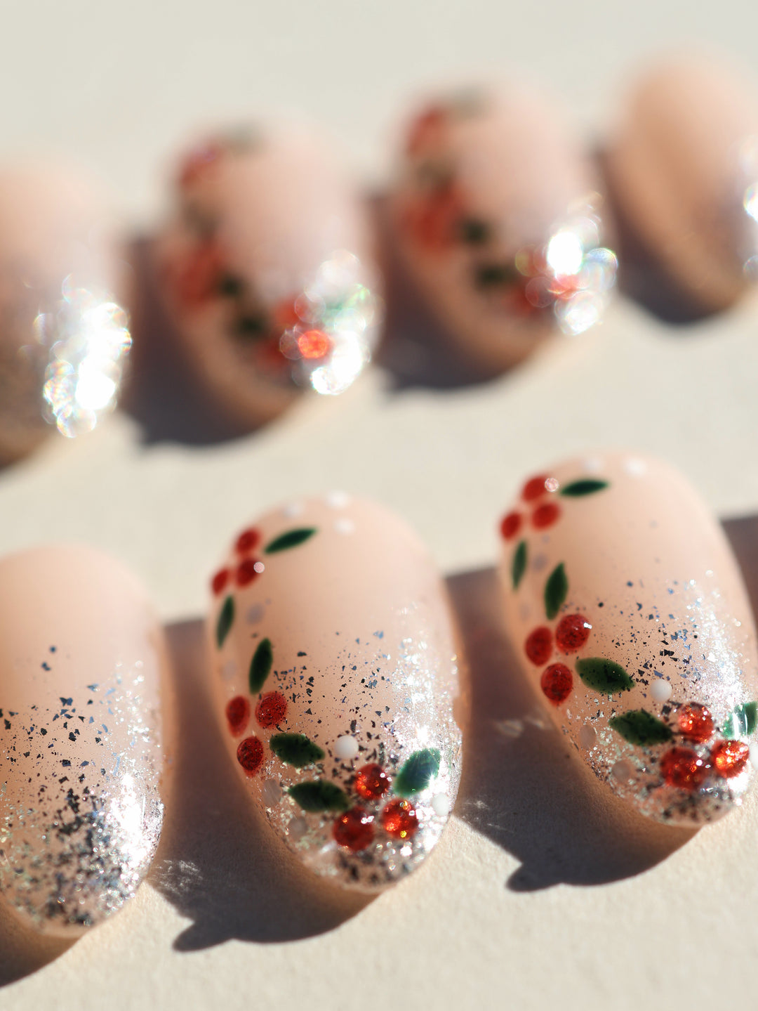 Berry Frost Christmas-themed press-on nails close-up with nude base, silver glitter gradient, red berries and green leaves.