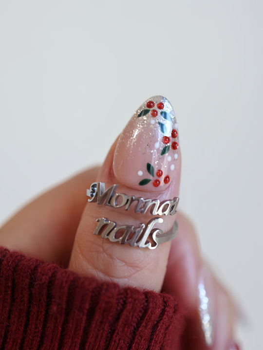 Berry Frost Christmas-themed press-on nails close-up worn on thumb with silver glitter, holly berries, leaves, and ruby rhinestones.