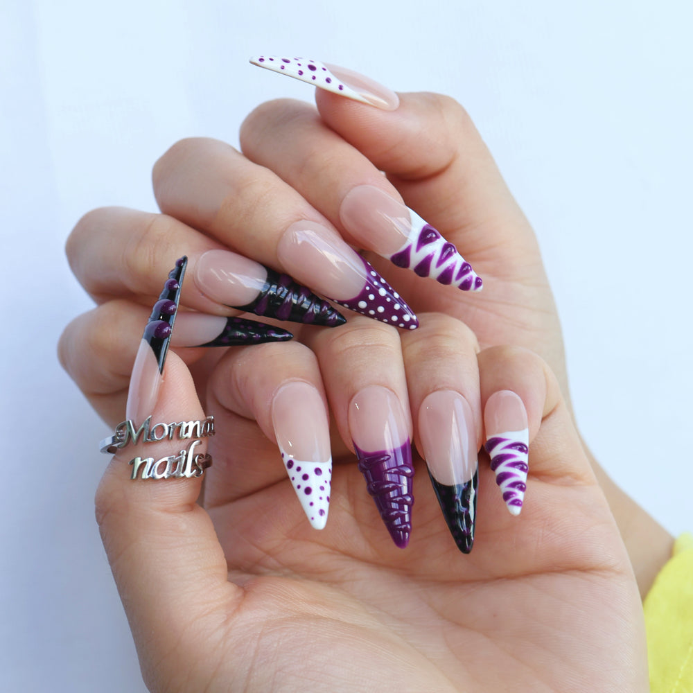 Berry Spin press-on nails on hand with nude base, purple polka dots, black French tips, and glossy 3D swirl accents