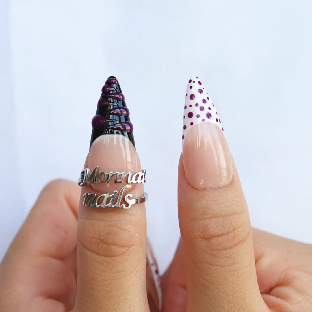 Berry Spin press-on nails worn on hands, with sheer nude bases, purple polka dots, and black French tip accents.