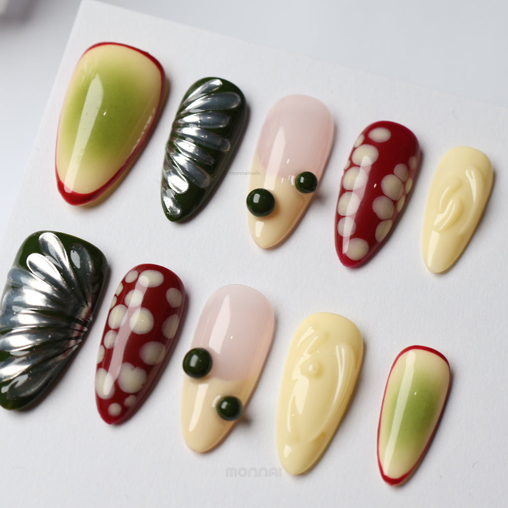 Berry press-on nails laid out in a playful mixed design with red, cream, nude and green abstract details