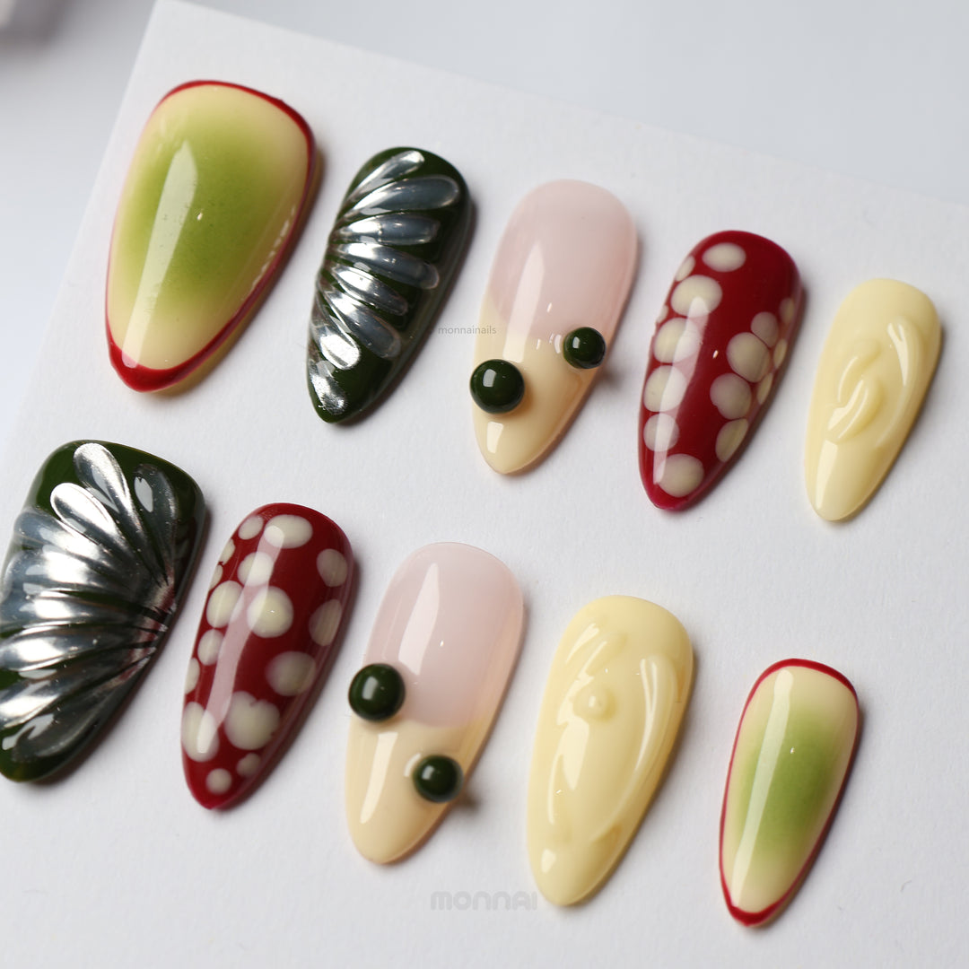 Berry press-on nails laid out in a playful mixed design with red, cream, nude and green abstract details