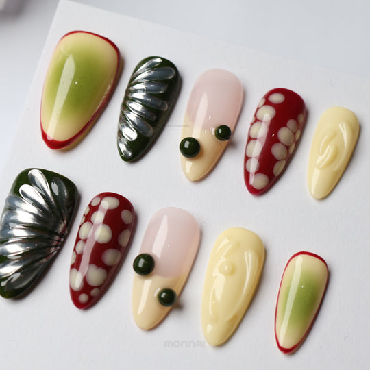 Berry press-on nails laid out in a playful mixed design with red, cream, nude and green abstract details