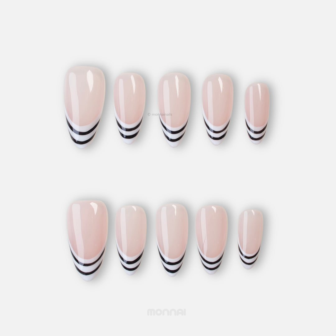 Black & White press-on nails laid out with nude pink bases and black-and-white striped French tips