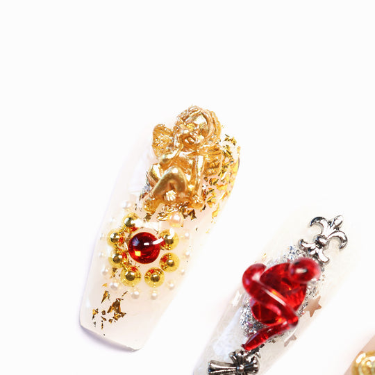 Blood Oath gothic press-on nails in close-up with gold cherub charm, ruby jewel, sacred heart motif and metallic framing