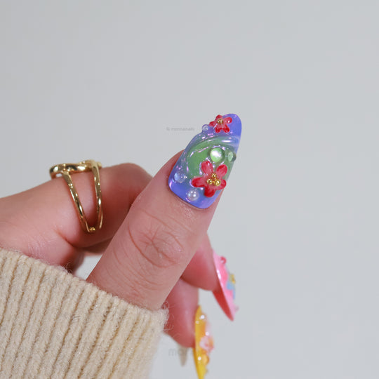 Blossom Fantasy press-on nails in close-up, showing pastel floral art, 3D flowers, and pearl dewdrops on lavender and green bases.