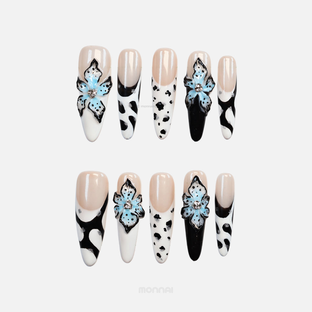 Blue Bloom press-on nails laid out in close-up with nude bases, black-and-white zebra and cow prints, and blue 3D flowers