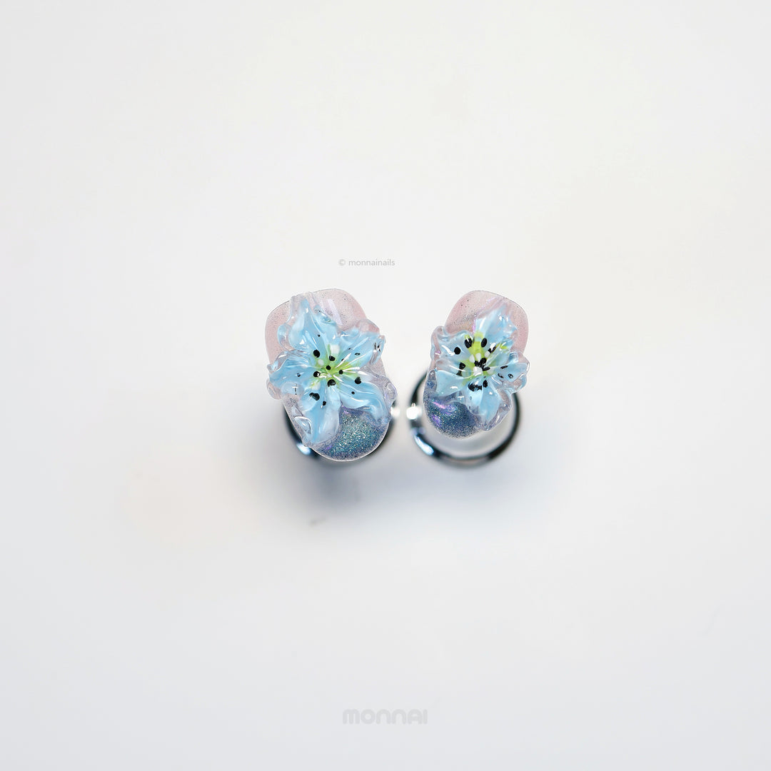 Blue Ice press-on nails with translucent blue 3D flowers, shimmer, and glossy cat-eye finish laid out in close-up