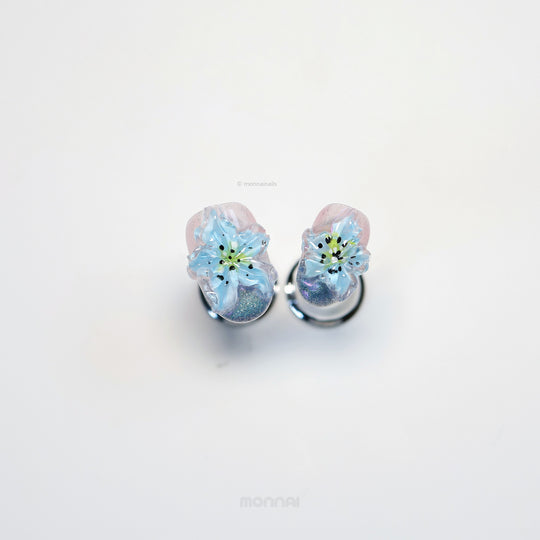 Blue Ice press-on nails with translucent blue 3D flowers, shimmer, and glossy cat-eye finish laid out in close-up