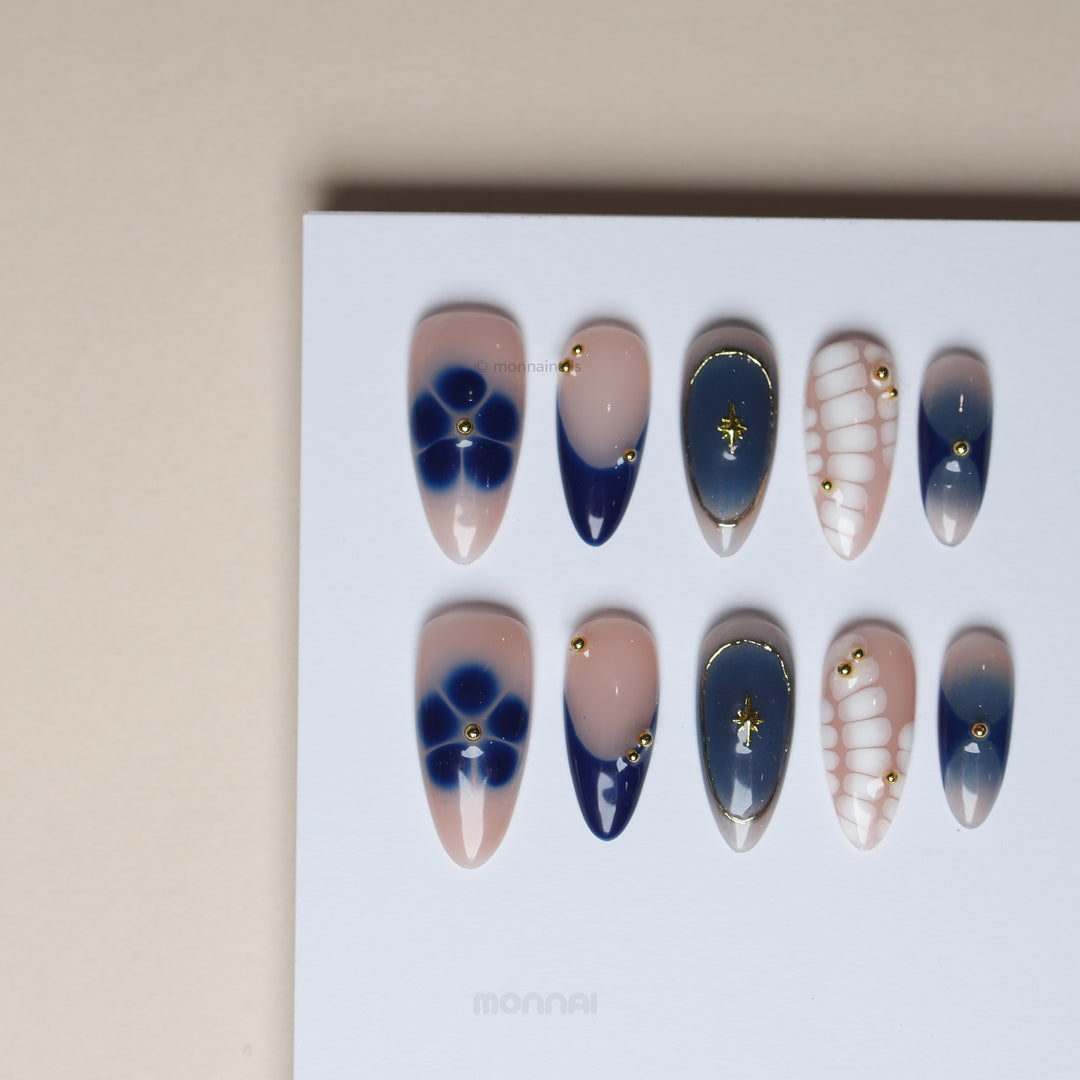 Blue Jasmine press-on nails laid out with navy French tips, floral accents, white crocodile pattern and gold charms