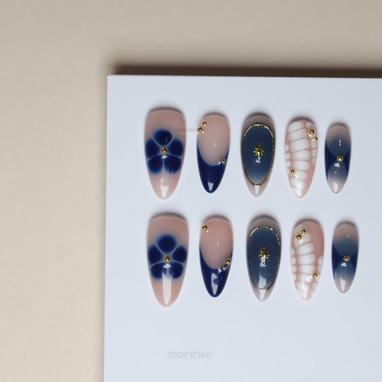 Blue Jasmine press-on nails laid out with navy French tips, floral accents, white crocodile pattern and gold charms
