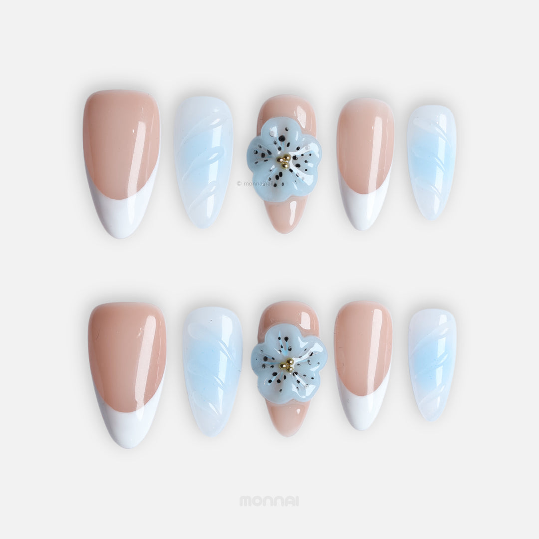 Blue Orchid press-on nails laid out, with soft nude, baby blue French tips and a 3D flower accent.