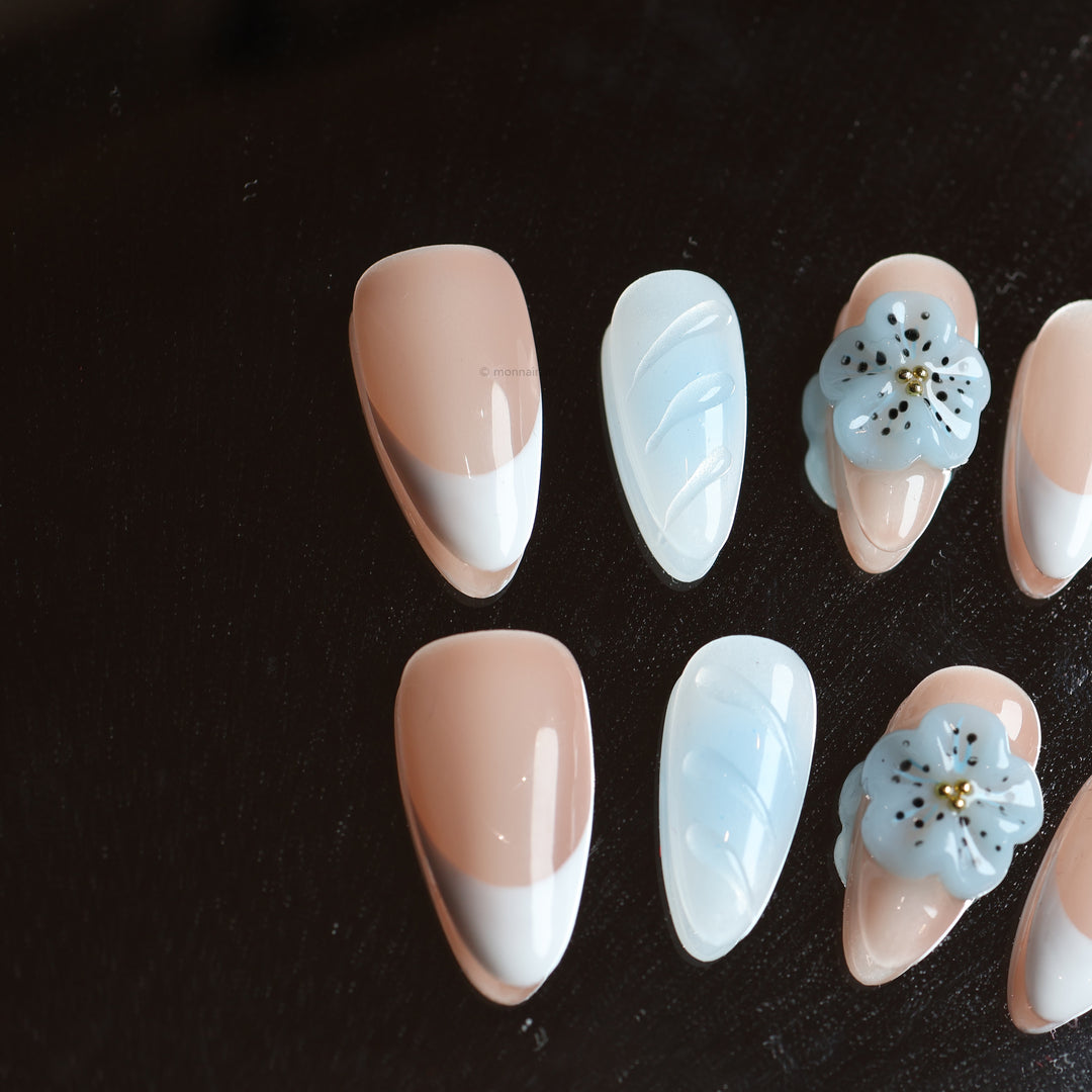 Blue Orchid press-on nails laid out in close-up, with soft nude, baby blue and crisp French tips plus a 3D flower.