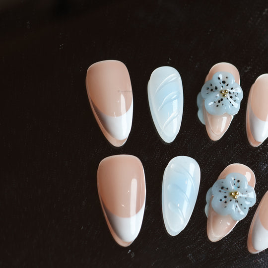 Blue Orchid press-on nails laid out in close-up, with soft nude, baby blue and crisp French tips plus a 3D flower.