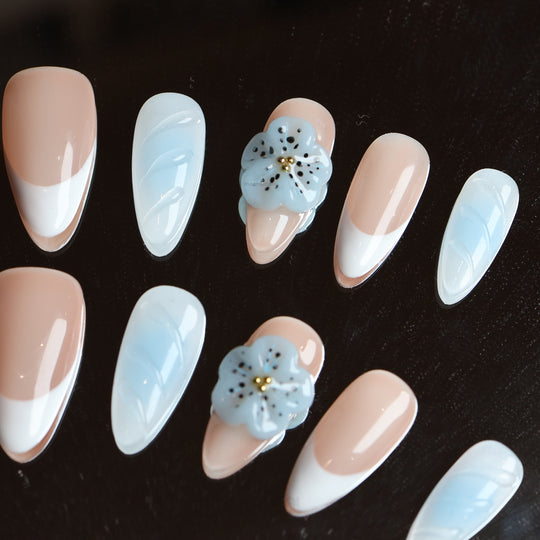 Blue Orchid press-on nails laid out with nude, baby blue French tips and sculpted 3D flower accents.