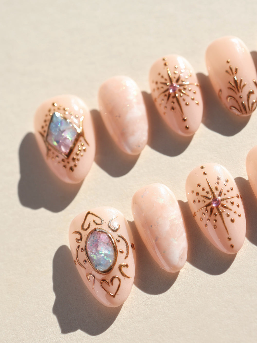 Blush Crown celestial press-on nails laid out with blush nude marbling, gold line art, and iridescent crystal accents
